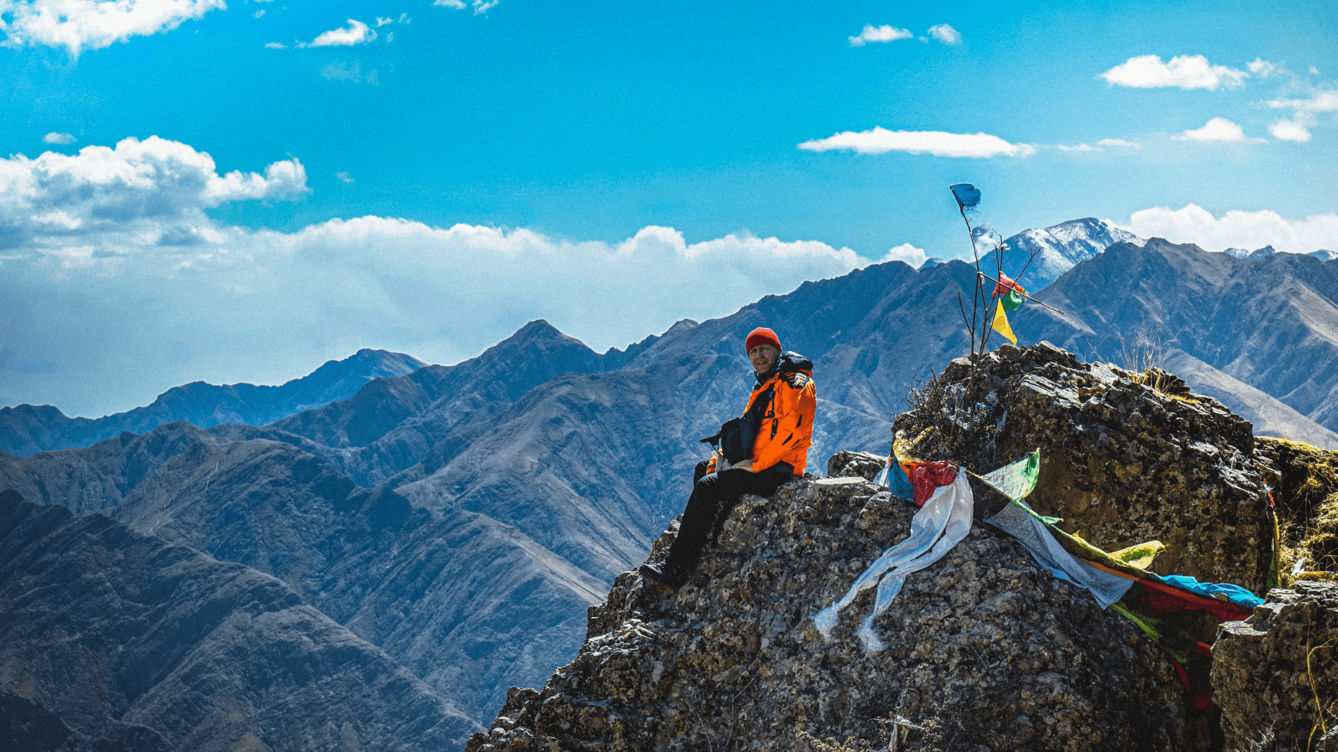 man in red jacket sitting on top of a mountain