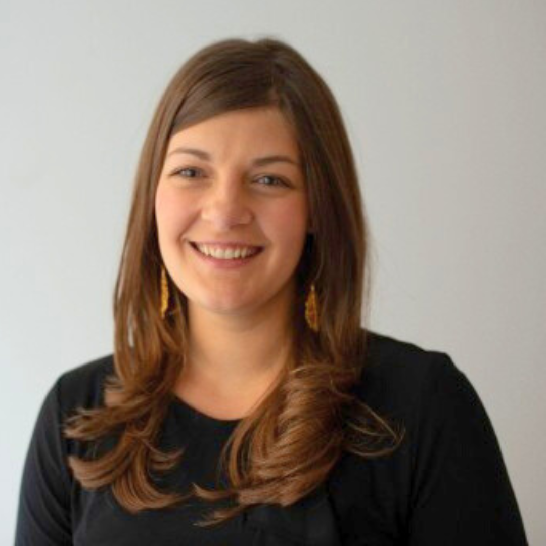 headshot of woman with long hair and black shirt in front of gray backdrop