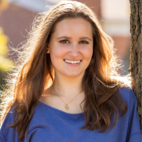 woman in blue shirt leans against a tree