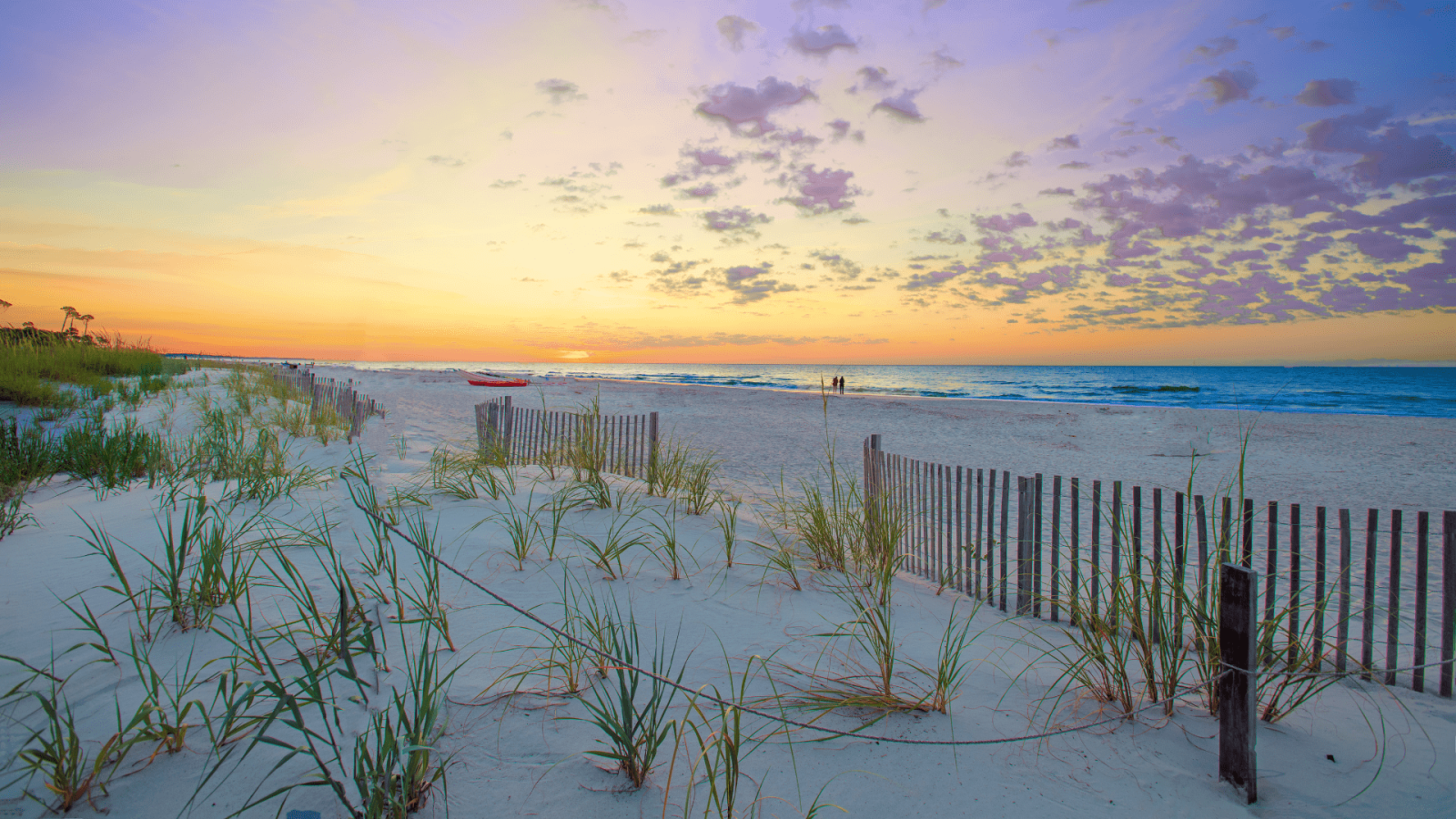 sandy beach with wood fence and beach grass at sunset